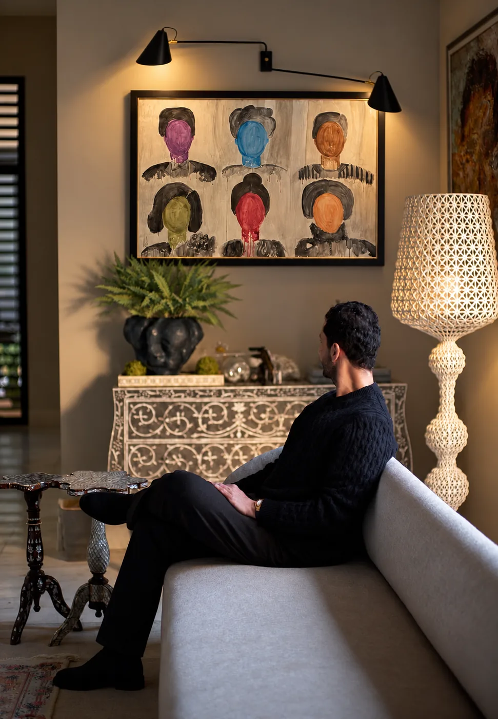 The artist at home, seated beneath a framed work of six faceless portraits